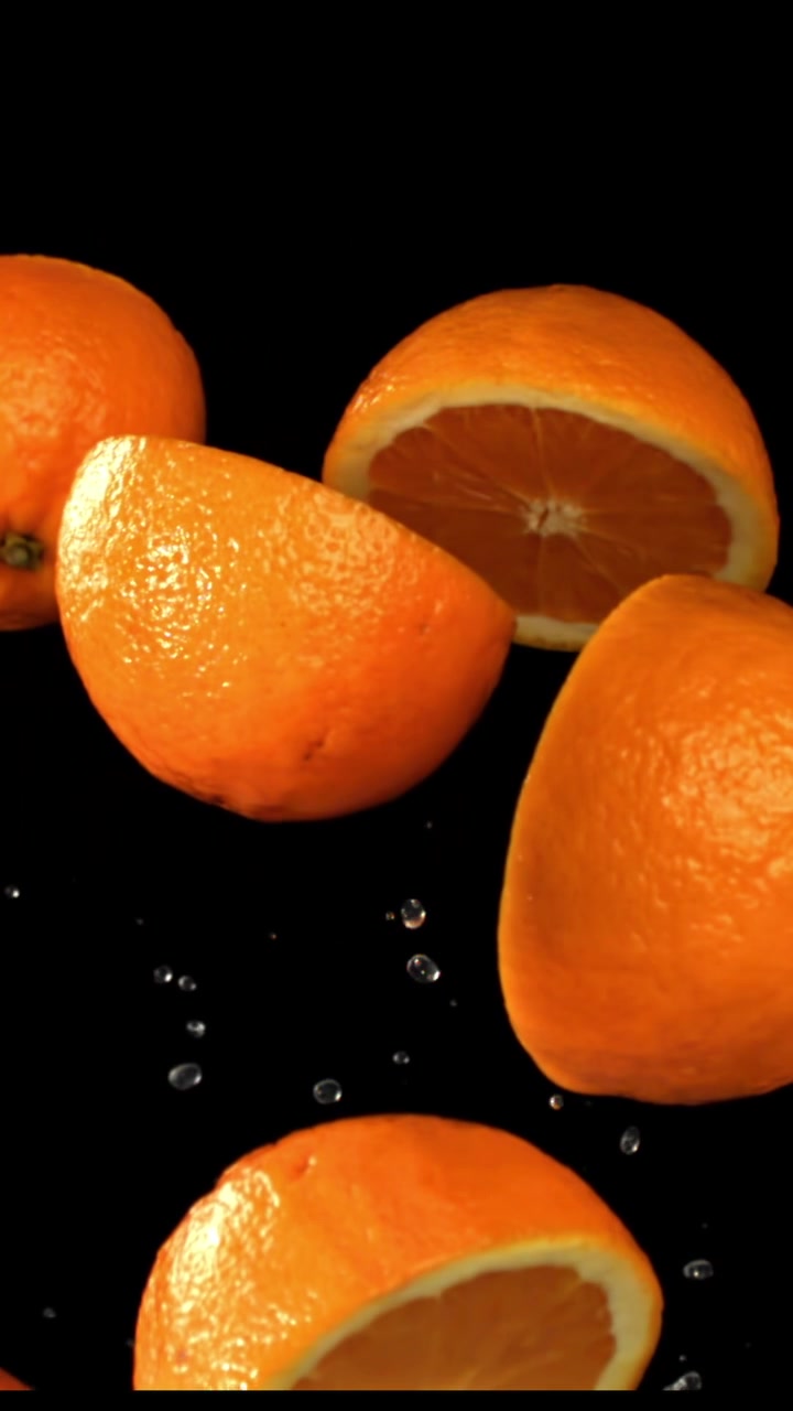 Arance fresche e mezze arance con goccioline d'acqua su sfondo nero