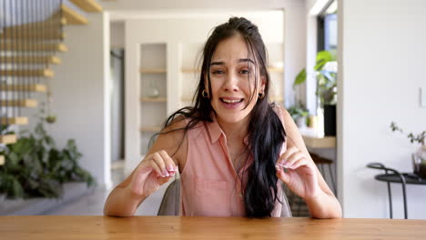 a young hispanic woman is sitting at a wooden table, on video call at home