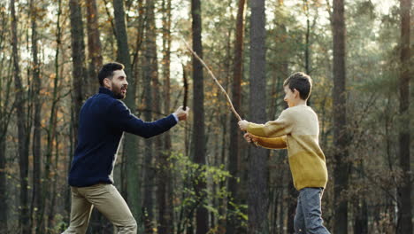 cheerful caucasian father and little son playing in the forest with sticks like they fighting with swords