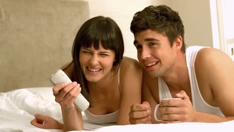 Happy-young-couple-watching-tv-lying-on-bed