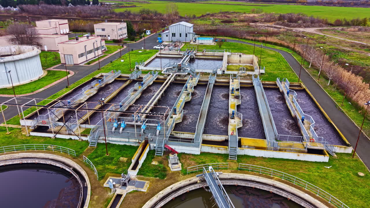 Water treatment facility located in a rural area showing large tanks and processing units against a vast green field backdrop