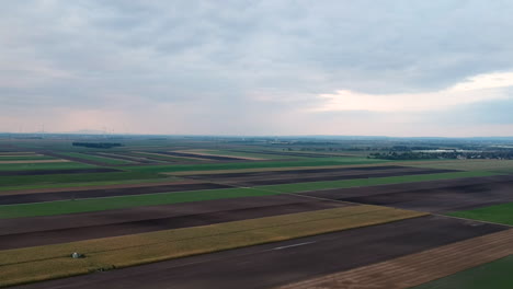 Toma-Aérea-De-Campos-Agrícolas-Verdes,-Amarillos-Y-Marrones-En-Europa-Durante-La-Puesta-De-Sol