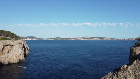 drone slowly moving into a island an ocean scene in 4k with rock formations to the left and right on a sunny day in mallorca spain