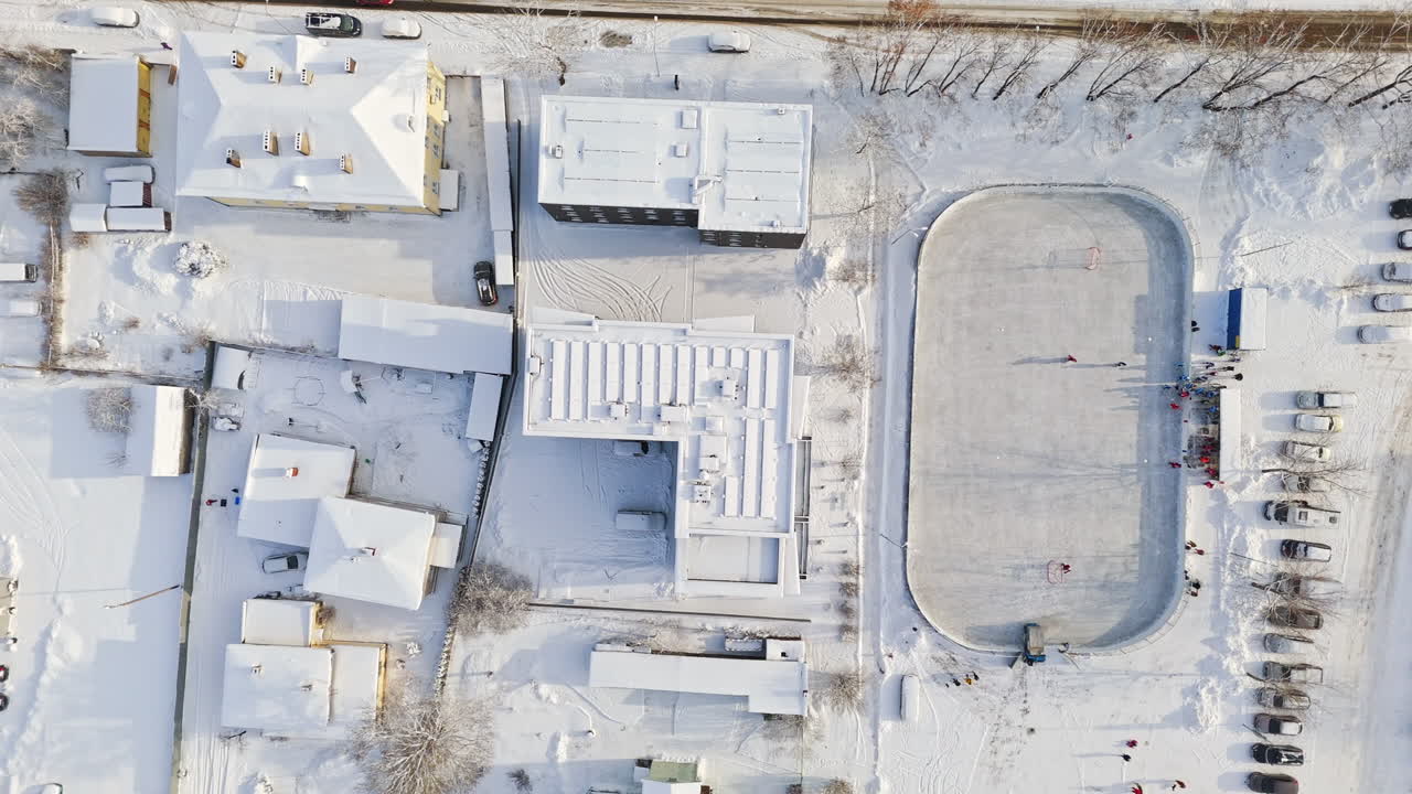 Birds eye drone shot over a ice hockey rink and snowy roofs, sunny, winter day