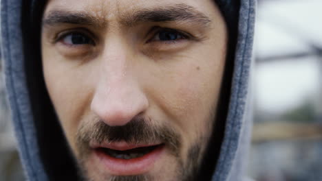 close-up view of the sweaty face of the male boxer in grey hoodie during a training outdoors an abandoned factory on a cloudy morning