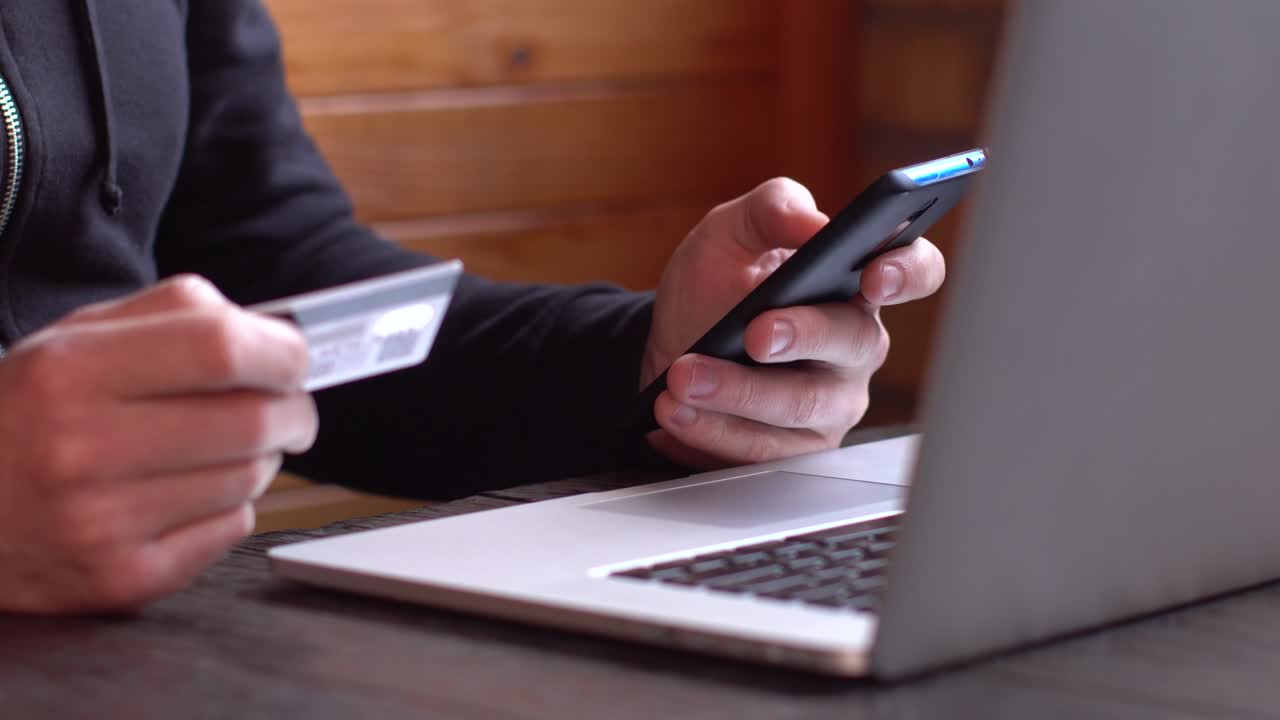 hombre de negocios con una sudadera negra haciendo pagos en línea con tarjeta de crédito y teléfono inteligente, compras en línea