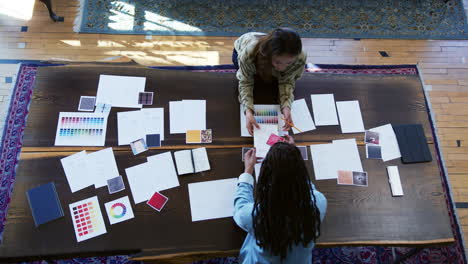 overhead view of two women having creative design meeting around wooden table in office