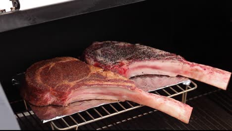 two raw tomahawk steaks seasoned and spice rub on the smoker grill tilt up concept: bbq, smoker, outside grilling, food preparation cookout, meat, ribs steaks