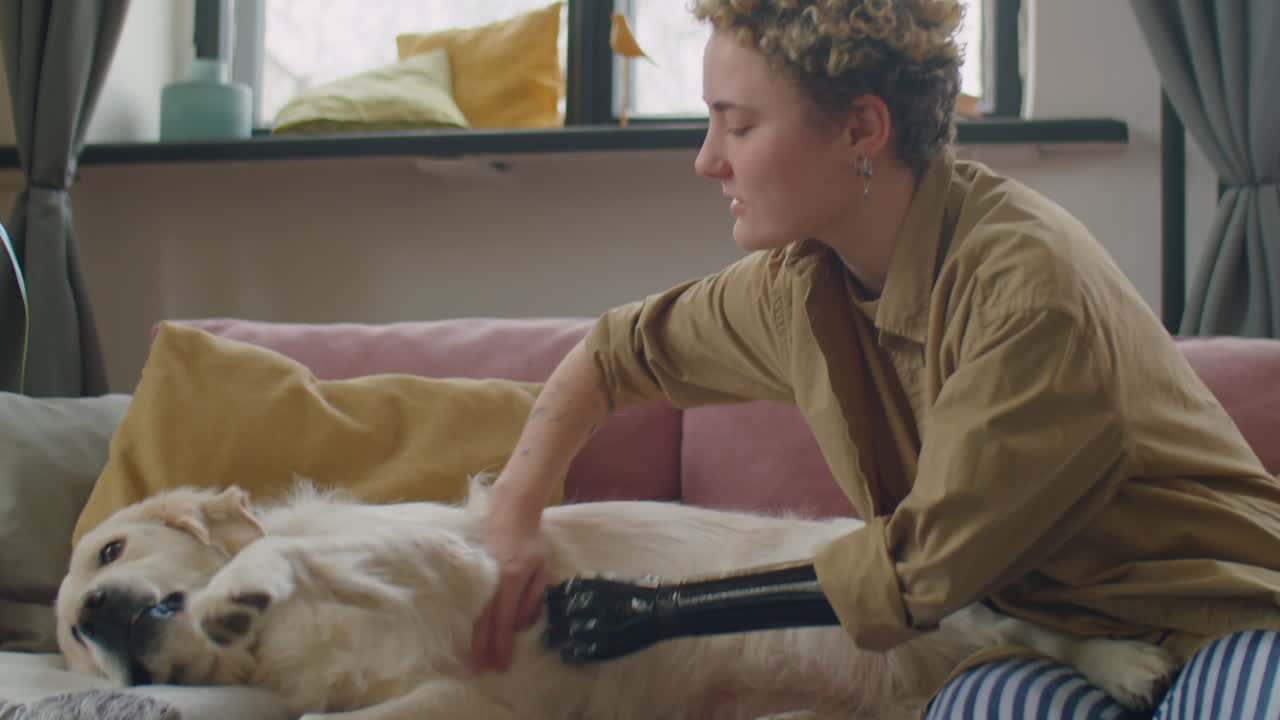Woman with Prosthetic Arm Petting Dog on Sofa at Home
