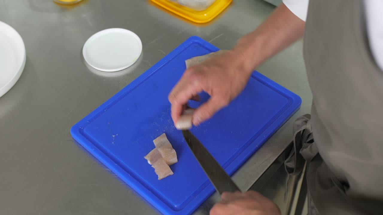 el hombre corta la carne de pescado en pedazos en el mostrador de metal en la cocina, vista de arriba hacia abajo