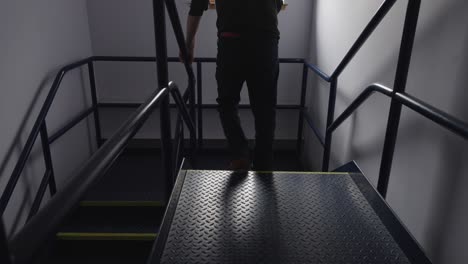 Man-at-work-walks-down-dark-lit-stairs-distressed-and-he-hits-railing