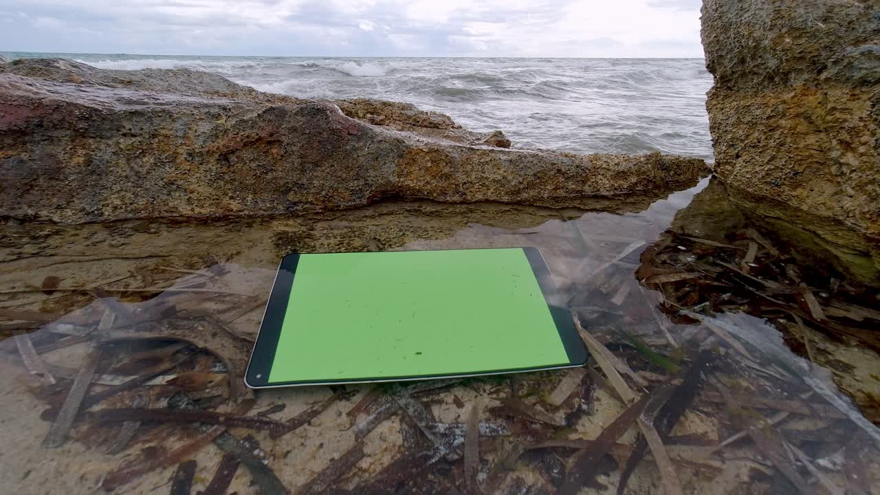 Electronic tablet with green screen floating in sea puddle