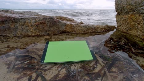 Electronic-tablet-with-green-screen-floating-in-sea-puddle