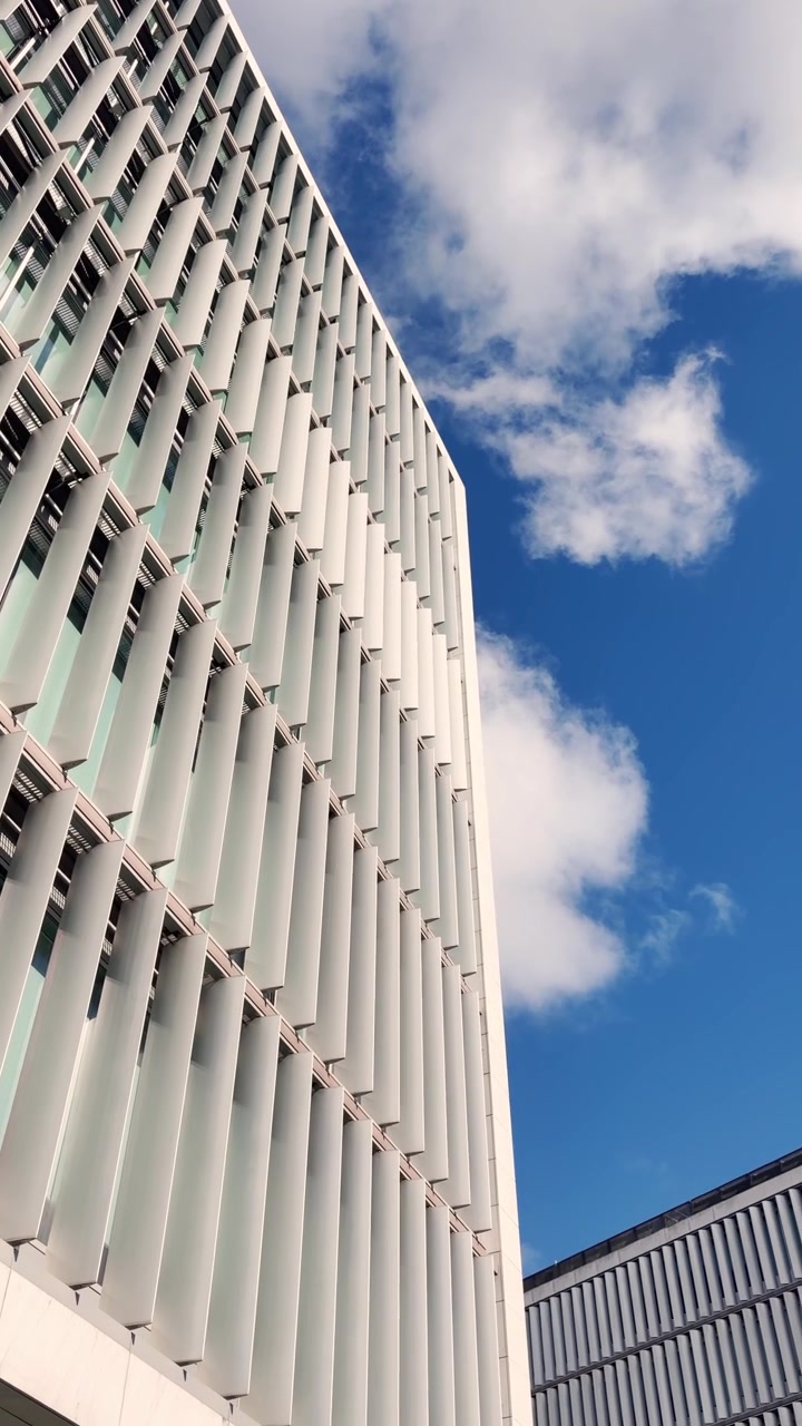 POV da fotocamera del telefono sulla facciata di un edificio per uffici aziendali in una giornata di sole all'aperto. Inquadratura di apertura con vista esterna della sede aziendale o di un centro direzionale/commerciale dal design moderno. UGC verticale