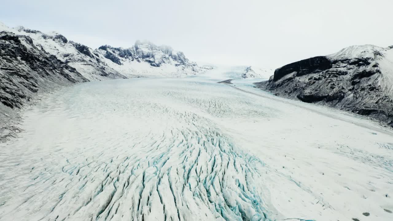 A sweeping view of Svinafellsjokull glacier’s icy surface merging with a muddy lagoon, framed by snow-dusted cliffs in Iceland’s wilderness.