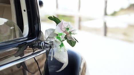 slow motion handheld panning shot of a rose with bow attached decoration to a black vintage car during a wedding between bride and groom