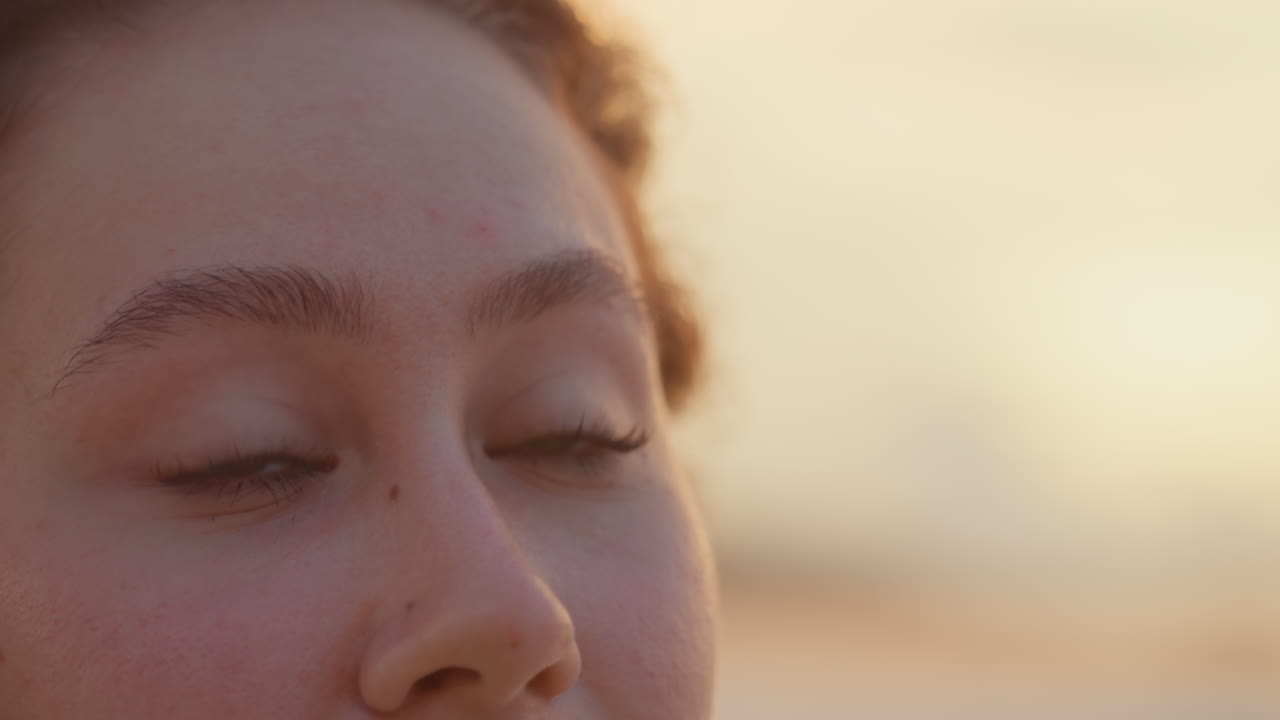 Nærbilde øyportrett kvinneøyne rolige, myke øyelokk og øyevipper fanger varmt lys, fjernt havglød, ettertenksomt uttrykk og diskret smil, intim filmatisk detalj og stille optimisme.