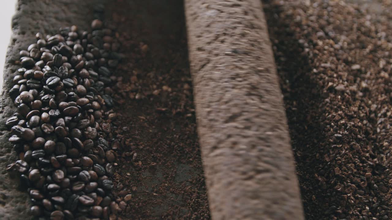 화산석에 있는 록 롤러로 커피 콩을 천천히 갈고 있는 사람의 슬로우 모션 탑 뷰