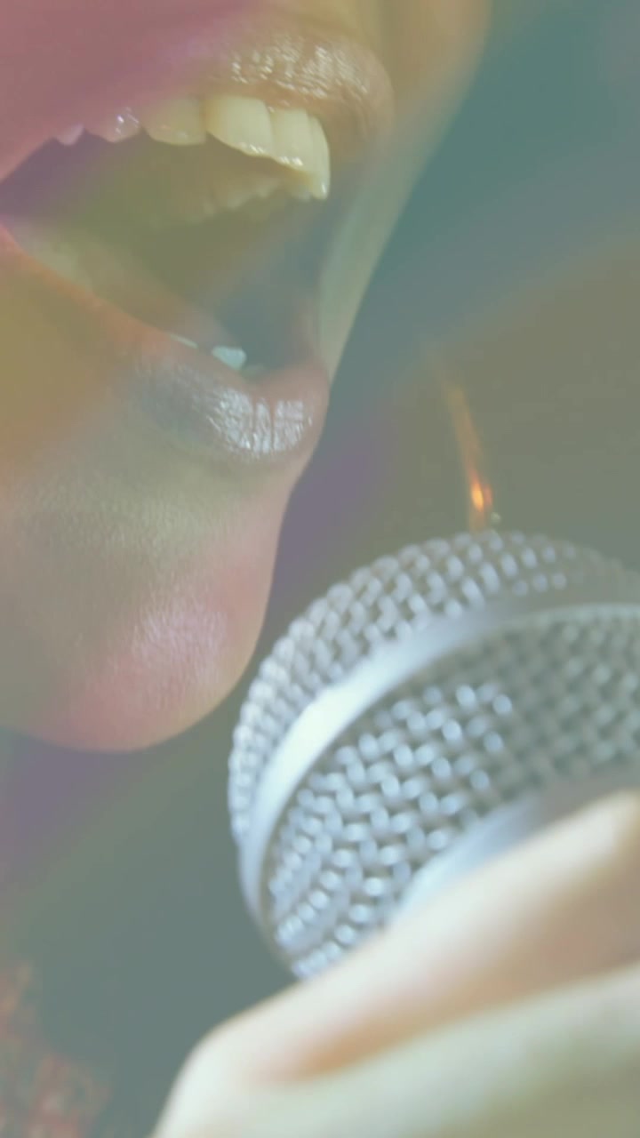 Video di una cantante afroamericana che usa un microfono, sotto luci colorate.