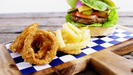 Hamburger,-onion-ring-and-french-fries-on-chopping-board