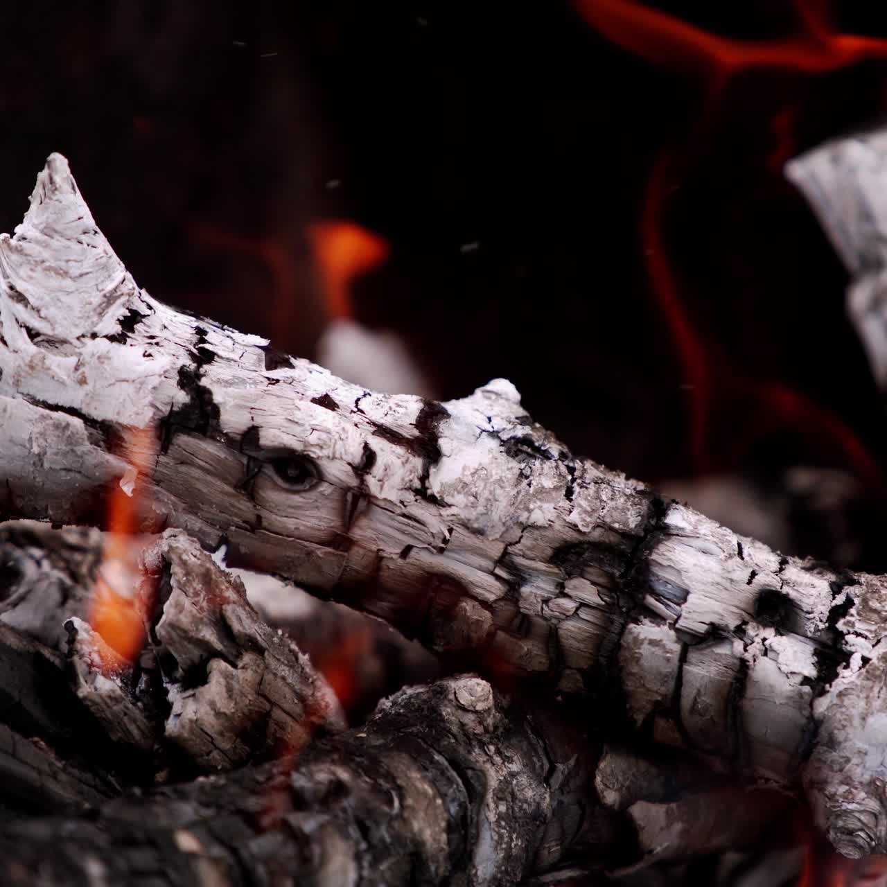 Glowing logs with smoke in fire. Hot embers of wooden logs burning on dark background. Close-up.