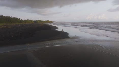 Mujer-Corriendo-En-La-Impresionante-Playa-De-Arena-Negra-De-Bali,-Antena-Cinematográfica---Pasión-Por-Los-Viajes