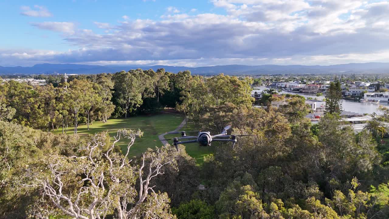 Aerial view of lush parkland with a drone hovering above, capturing expansive greenery and distant cityscape under soft daylight