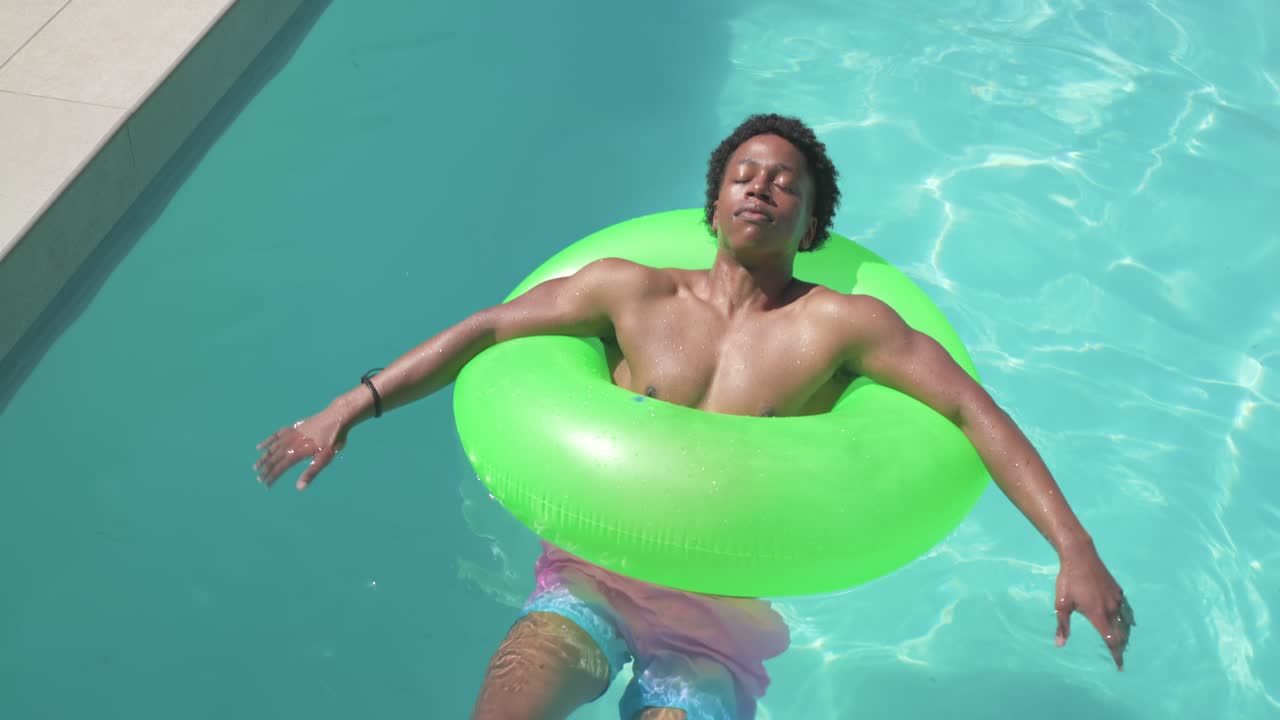 African American man settling into bright green ring, floating and splashing to relax in pool