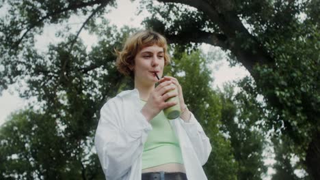 una mujer joven disfrutando de un batido en un parque.