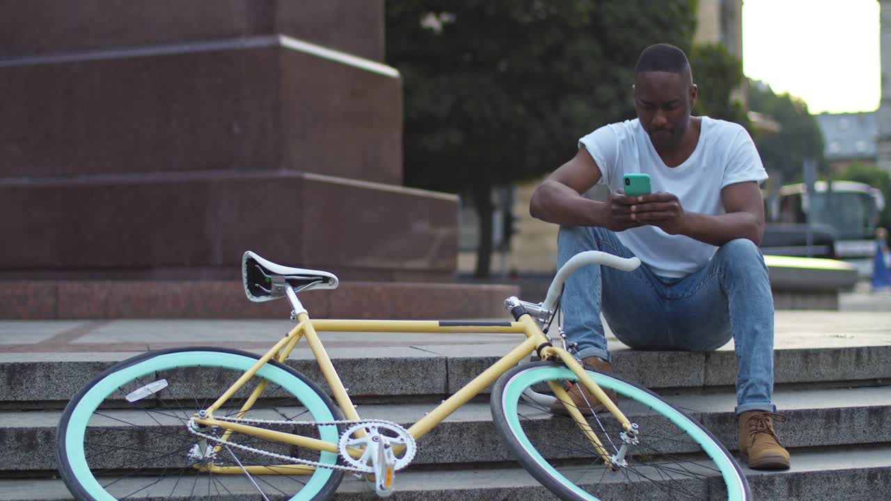 Ein Mann mit einem Fahrrad sitzt auf einer Treppe und benutzt ein Handy