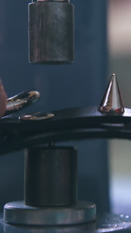 cu: professional designer sets metal accessory spikes on fashionable black leather choker with press machine closeup