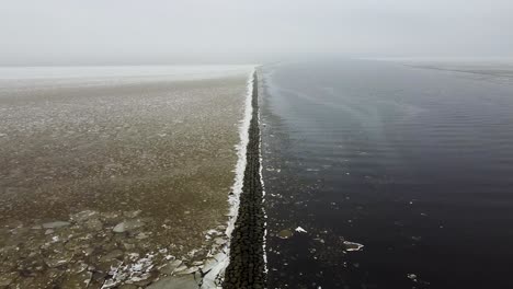 rising aerial drone view of a long stone sea mole breakwater in winter