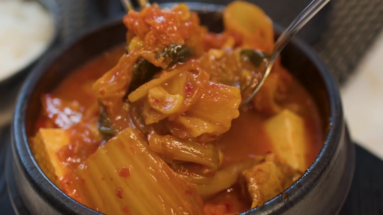 Gros plan sur des ustensiles en métal remuant une marmite bouillonnante de ragoût épicé de kimchi jjigae rouge