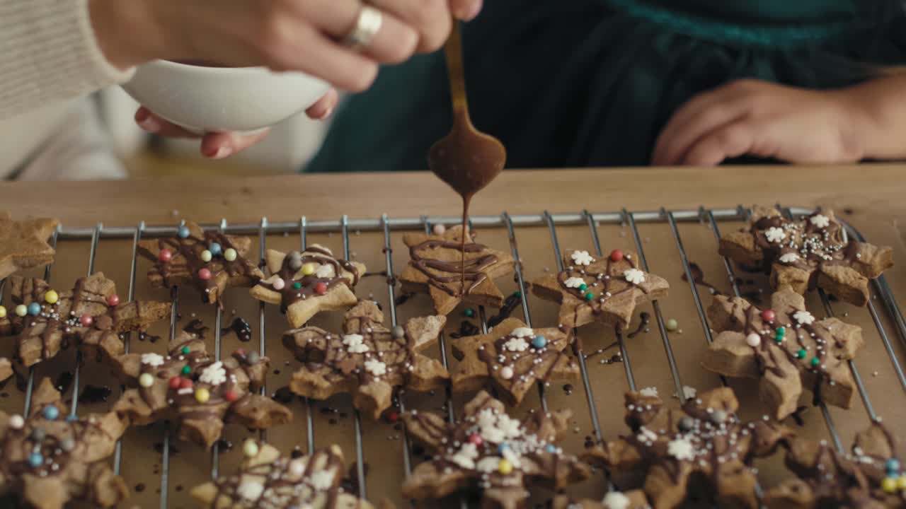 detalle de una madre y una hija caucásicas decorando galletas de pan de jengibre con chocolate y salpicaduras.
