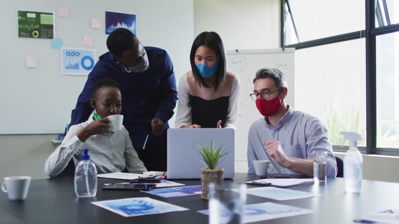 Office colleagues wearing face masks using laptop together in meeting room at modern office