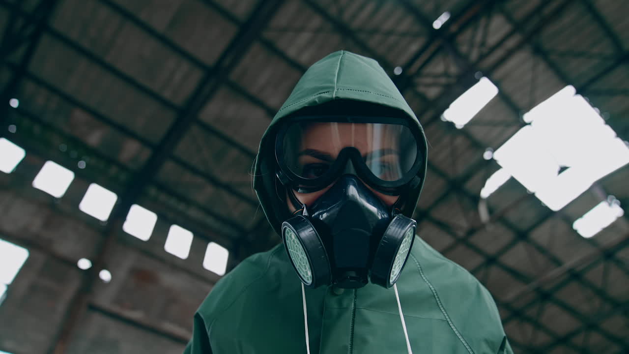 Person in safety chemical suit looks at camera. Portrait of a human in gas mask on ruined building background. View from below. Polluted zone. High level of radiation.