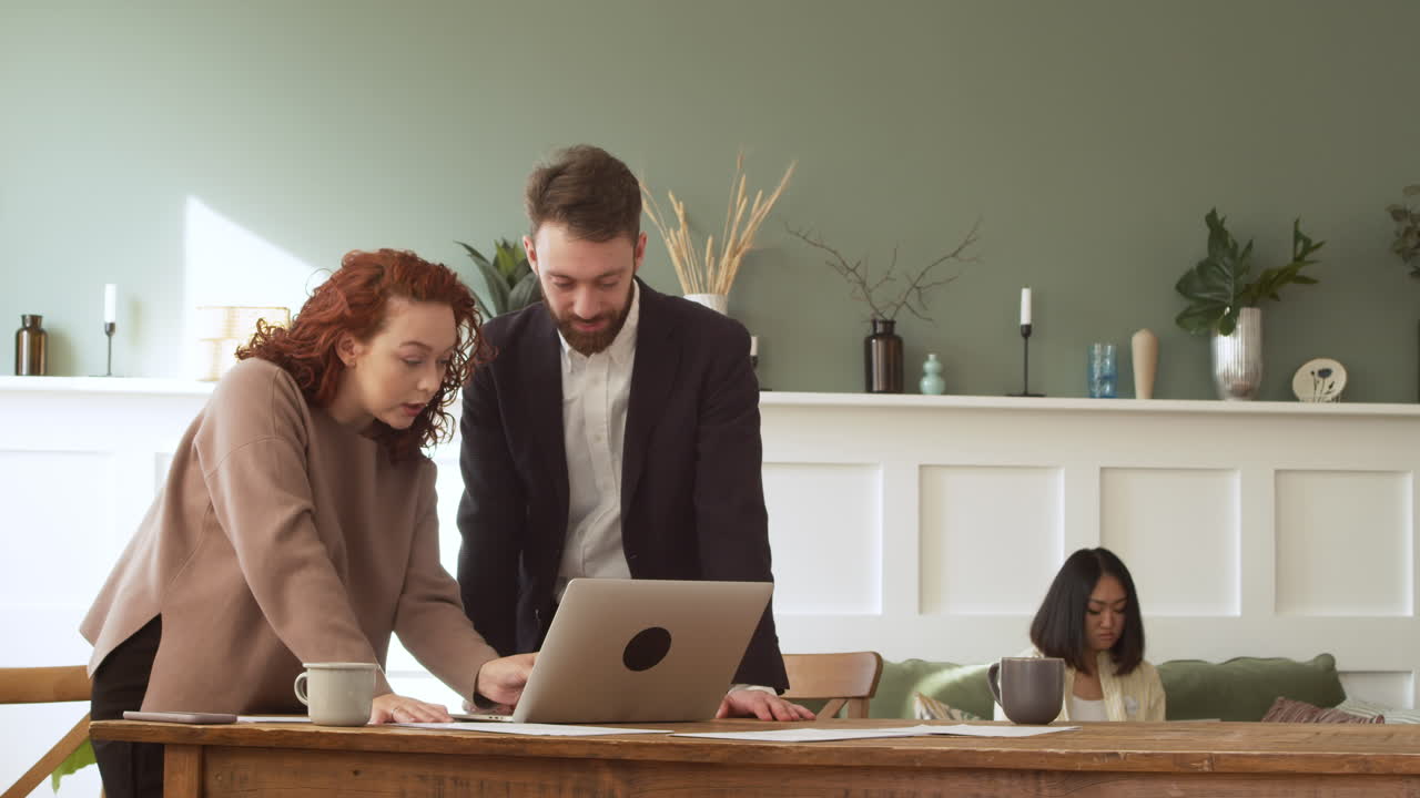 mujer y hombre de pie en la mesa, debatiendo y mirando la computadora portátil