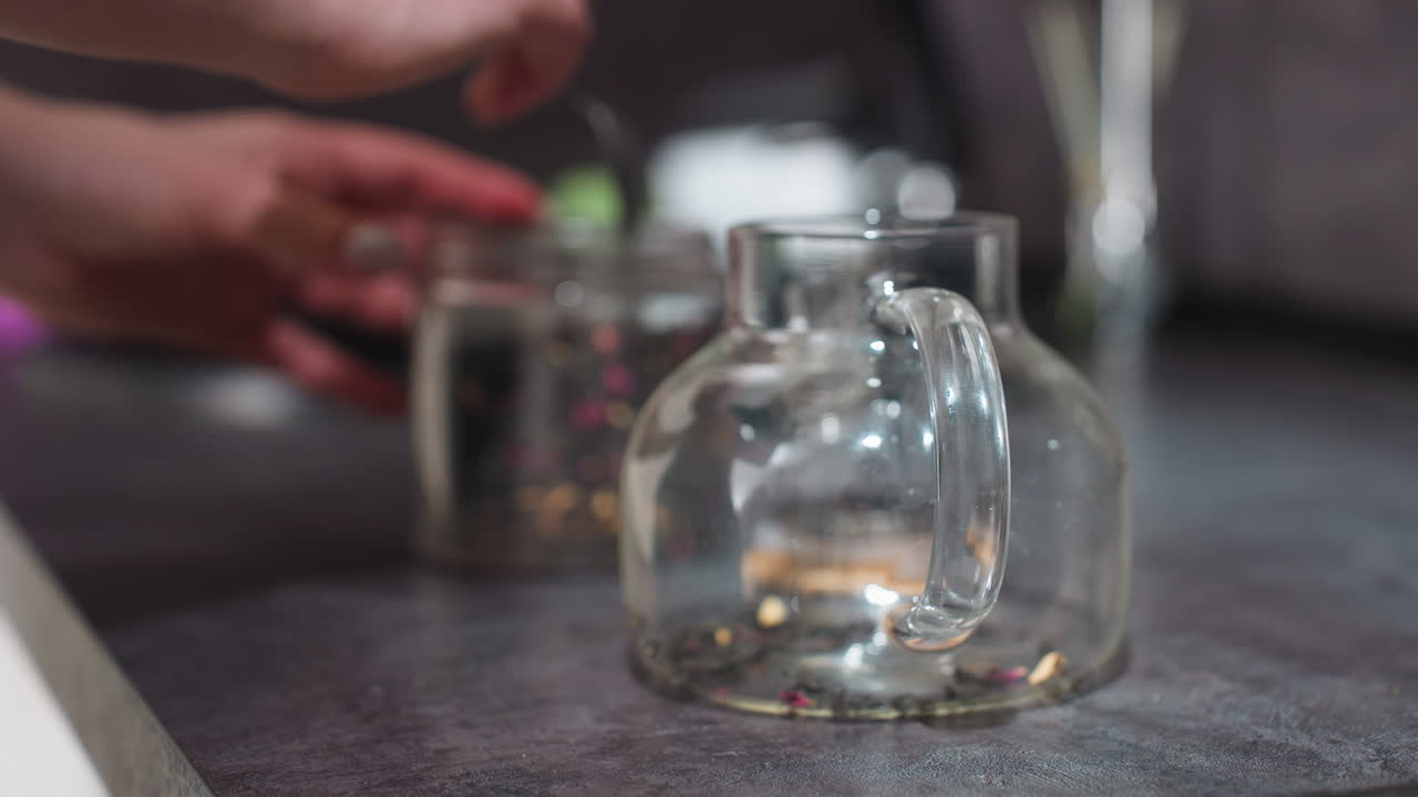 Teiera di vetro con foglie di tè sfuse che si depositano sul fondo, luce calda della cucina, profondità di campo ridotta, infusione lenta, foschia di vapore, superficie riflettente, macro ravvicinata sulla consistenza delle foglie e sulla tinta ambrata, atmosfera meditativa e accogliente