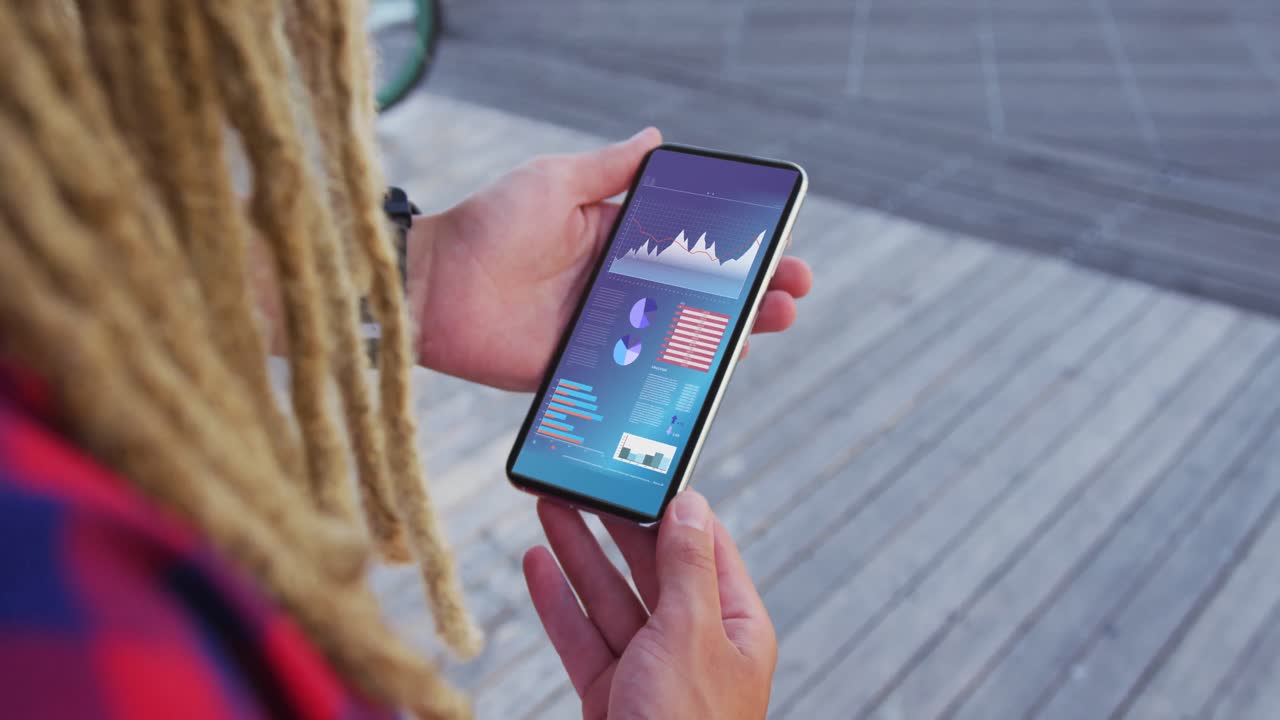En kaukasisk mands hænder med dreadlocks bruger en smartphone med statistik på skærmen