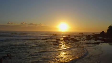 aerial shot moving into a golden sunrise over beach and rocks in springtime near port macquarie beach