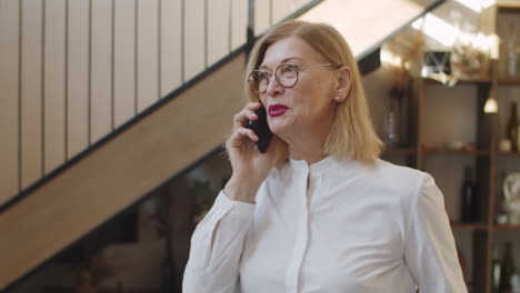 mujer de negocios sénior caminando en la oficina y teniendo una conversación telefónica