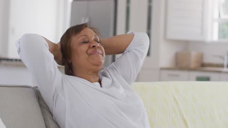 feliz mujer mayor afroamericana reclinada en el sofá con los ojos cerrados, sonriendo