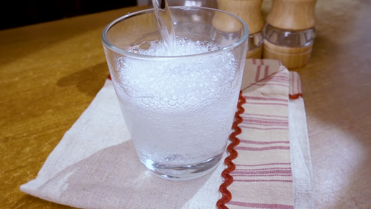 Acqua minerale che si versa in un bicchiere, la colazione del mattino. Slow motion con ripresa a tracciamento rotazionale