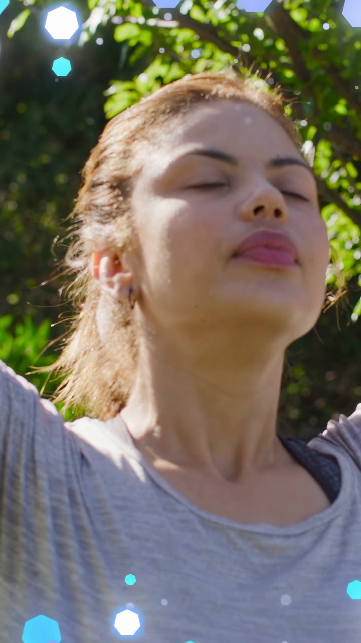 Video verticale: Donna che inspira alzando le braccia in giardino per fare yoga, con bokeh blu che fluttua sul petto.