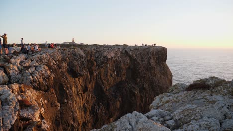 Establecimiento-De-Tiro,-Gente-Reunida-Cerca-Del-Borde-De-Un-Acantilado-Rocoso-En-El-Algarve,-Portugal,-Vista-Panorámica-Del-Mar-Y-Amanecer-En-El-Fondo