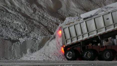 camión volquete descargando un montón de nieve durante la noche después de una tormenta de invierno