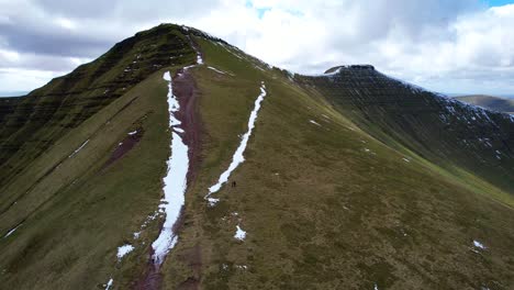 Aerial-flying-above-mountain-towards-snowy-peak-of-Pen-y-Fan-in-Wales,-UK