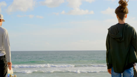 rear view of young caucasian men standing on the beach and looking at sea 4k