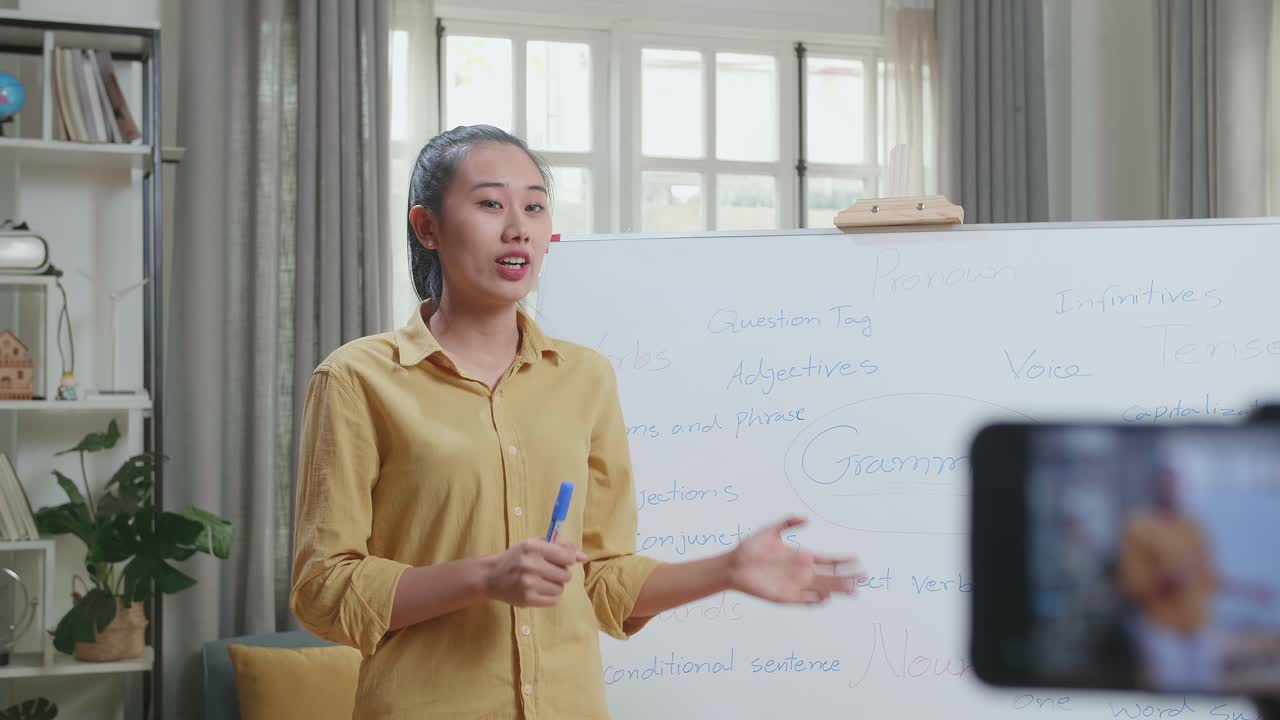 Asian Female Teacher With Marker Pen Shoots Video By Smartphone Camera While Teaching English At Home