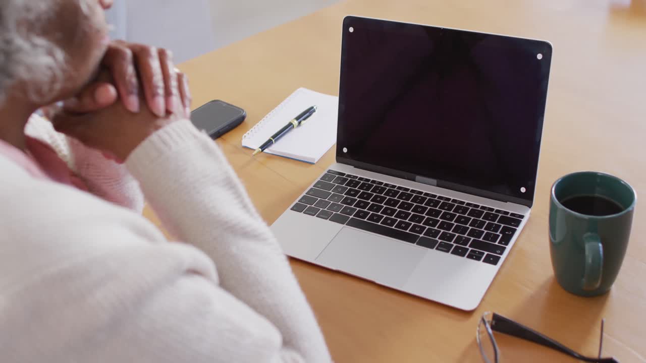 retrato de una mujer afroamericana anciana sentada en una mesa, usando una computadora portátil con copyspace.